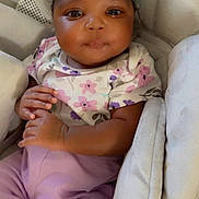 Kamia is registered to the contest to win money with this photo: baby, child, infant, headband, bow, floral_shirt, purple_pants, cushion, baby_seat, cute, portrait, indoor, hands, eyes, smile, clothing, person, soft, comfort, young