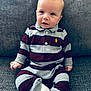 baby, child, striped_clothing, cast, foot_cast, couch, gray_couch, sitting, curious_expression, indoor, portrait, infant, casual_wear, long_sleeves, pants, knitted_fabric, young_child, one_person, seated, cozy