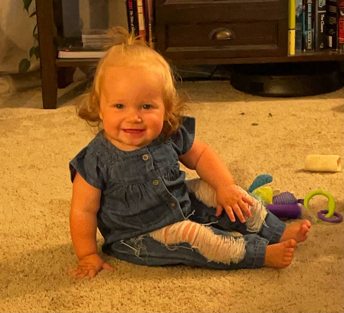 Jemma is registered to the contest to win money with this photo: automotive_tire, baby, baby_toddler_clothing, cheek, child, facial_expression, floor, flooring, foot, fun, happy, head, joy, nose, person, sitting, skin, smile, tire, toddler