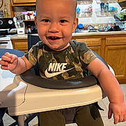 Myles is registered to the contest to win money with this photo: toddler, baby, high_chair, smiling, camouflage, nike, shirt, kitchen, cabinet, countertop, sink, plastic_bottle, child, furniture, indoor, person, happy, short_hair, table, seat