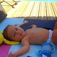 Nathan a rejoint le concours — aidez-le/la à gagner de superbes lots ! baby, towel, pool, toy, sippy_cup, diaper, wooden_deck, sunlight, relaxing, infant, outdoor, water, plastic_toy, blue, yellow, pink, clothing, bare_chest, child, summer