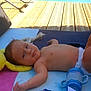 baby, towel, pool, toy, sippy_cup, diaper, wooden_deck, sunlight, relaxing, infant, outdoor, water, plastic_toy, blue, yellow, pink, clothing, bare_chest, child, summer