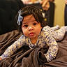 Lina Rose is registered to the contest to win money with this photo: baby, infant, child, blue_bow, floral_outfit, tongue_out, bed, blanket, curly_hair, indoors, soft_lighting, portrait, cute, playful, person, young_child, face, expression, crawling, cozy