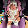 baby, infant, car_seat, purple, floral_hat, floral_dress, smiling, toy, white_socks, cute, child, seatbelt, comfortable, indoor, closeup, adorable, happy, small_hands, headwear, portrait