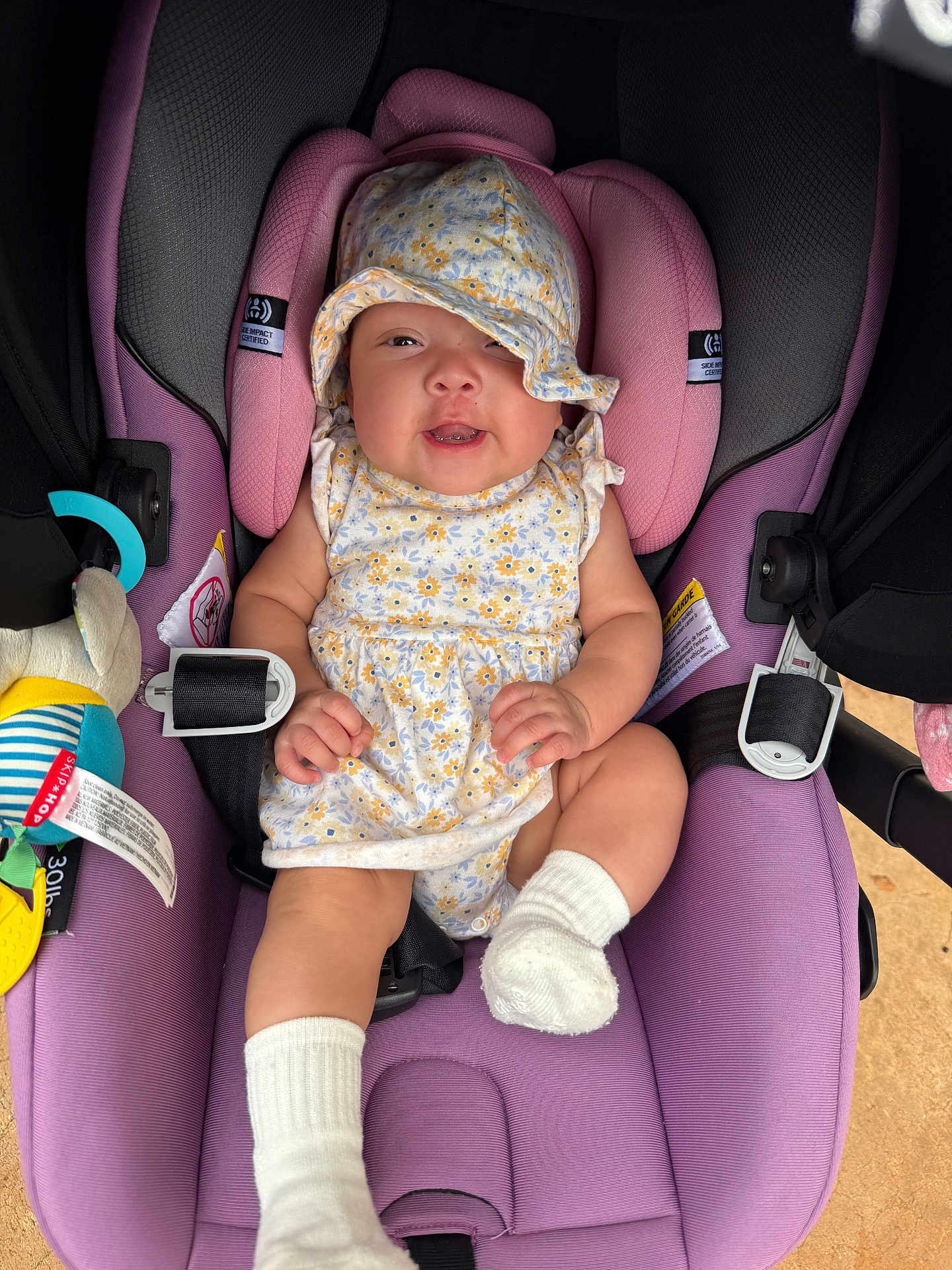 Amaryllis Perez is registered to the contest to win money with this photo: baby, infant, car_seat, purple, floral_hat, floral_dress, smiling, toy, white_socks, cute, child, seatbelt, comfortable, indoor, closeup, adorable, happy, small_hands, headwear, portrait