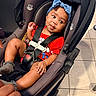 baby, child, infant, stroller, portrait, smiling, bow, headband, red_outfit, car_seat, harness, seated, indoor, tile_floor, footwear, hands, legs, happy, closeup, photography