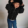 child, toddler, hooded_jacket, black_jacket, jeans, sneakers, standing, indoor, smiling, cute, fashion, casual, floor, wall, posing, young_child, portrait, happy, clothing, footwear