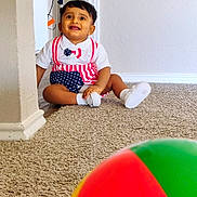 Olin is registered to the contest to win money with this photo: toddler, child, carpet, indoor, wall, fan, beach_ball, smiling, sitting, clothing, white_shoes, corner, room, floor, toy, playful, happy, person, home, casual