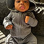 Dakari is registered to the contest to win money with this photo: baby, child, clothing, comfortable, couch, cozy, cute, expression, face, fist, gray_outfit, hooded_clothing, indoor, infant, person, portrait, shadow, sitting, sunlight, young_child
