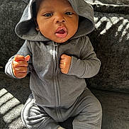 Dakari is registered to the contest to win money with this photo: baby, casual, child, couch, cozy, cute, expression, face, fist, gray_clothing, hoodie, indoor, infant, portrait, shadow, sitting, sock, sunlight, texture, young_child