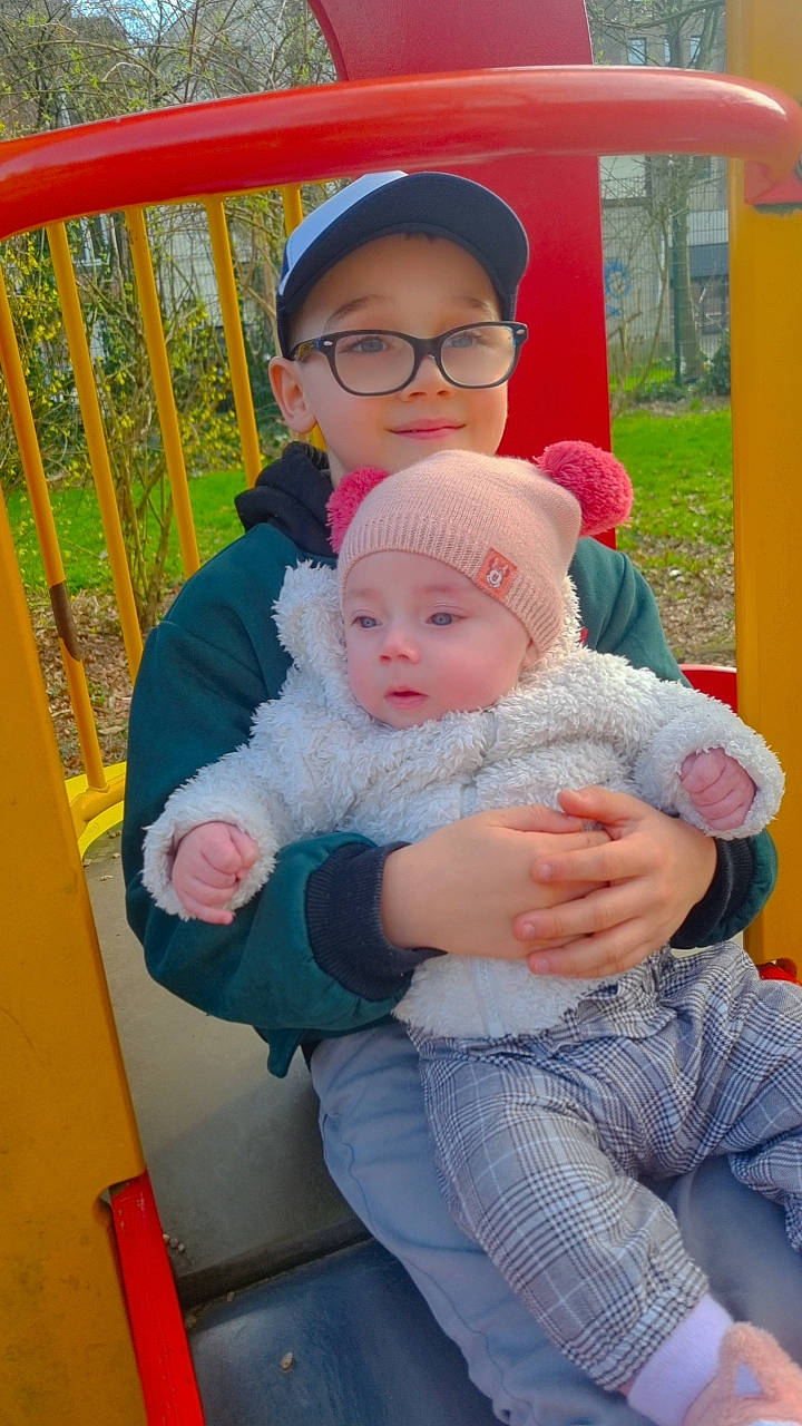 émyliana a rejoint le concours — aidez-le/la à gagner de superbes lots ! baby, baby_products, baby_toddler_clothing, baseball_cap, cap, child, eye, eyewear, facial_expression, fun, glasses, grass, happy, hat, headwear, lap, leisure, person, plant, recreation