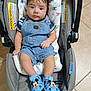 baby, infant, car_seat, denim_overalls, blue_sandals, mickey_mouse, blanket, alphabet, floor_tile, indoor, child, cute, footwear, person, sitting, clothing, soft_toy, head, face, portrait