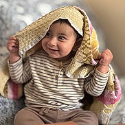 Gurniwaz joined the competition — help win amazing prizes! baby, blanket, brown_pants, child, clothing, cozy, cute, face, hands, happy, home, indoor, knitted, playful, portrait, sitting, smiling, soft_light, striped_shirt, toddler