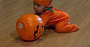 Chase is registered to the contest to win money with this photo: baby, child, costume, crawling, door, fan, festive, floor, green, halloween, headwear, holiday, indoor, infant, orange, person, plastic, pumpkin, toy, wooden_floor