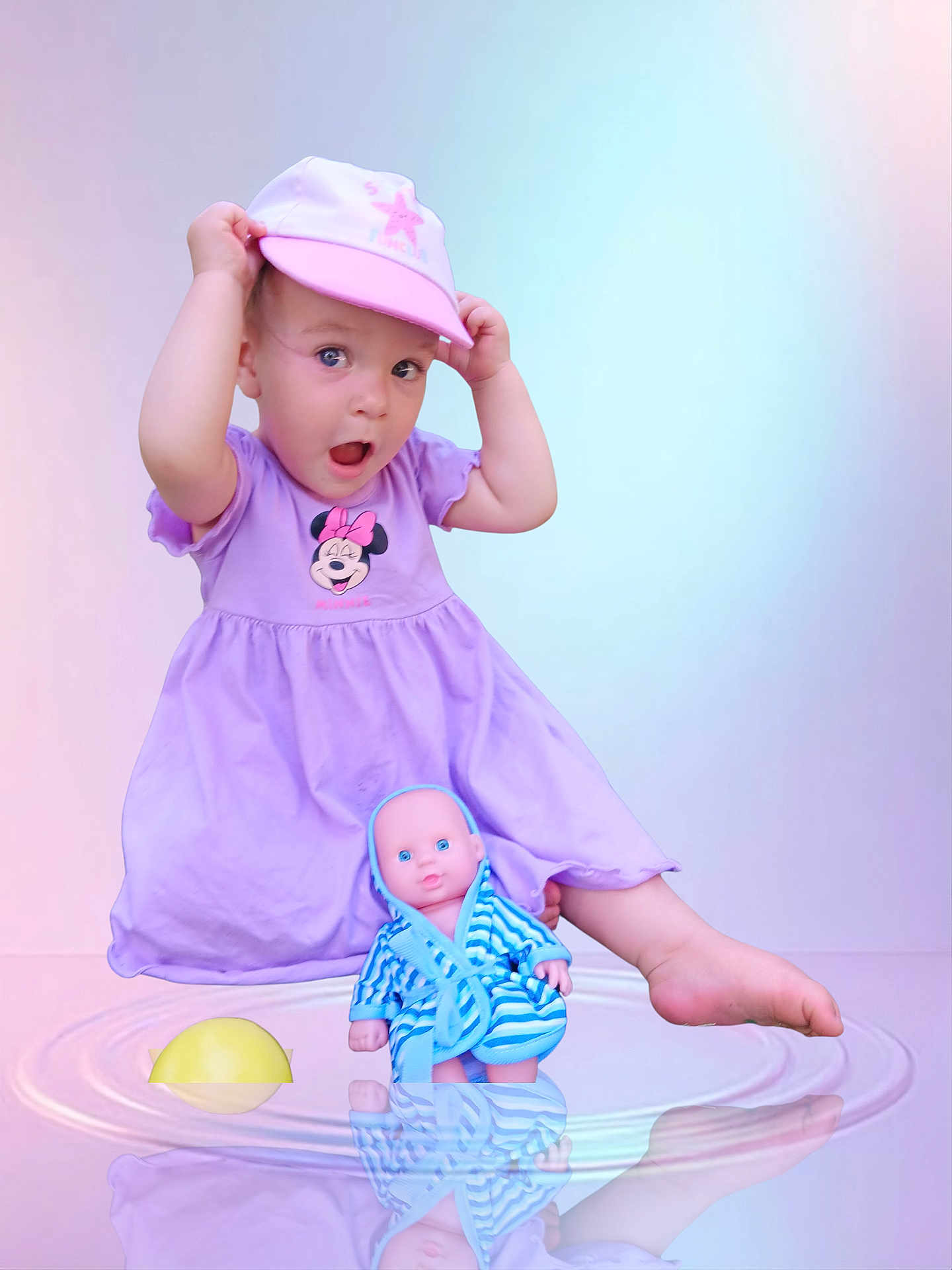 Ynnaïa a rejoint le concours — aidez-le/la à gagner de superbes lots ! blue, cap, child, cute, doll, dress, indoor, minnie_mouse, pastel_background, pink, playful, purple, reflection, robe, sitting, striped, surprised, toddler, toy, water_ripple