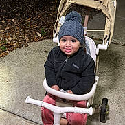 Nadine joined the competition — help win amazing prizes! toddler, child, tricycle, stroller, hat, jacket, smile, outdoor, night, concrete, footwear, pants, play, happy, person, toy, wheel, cold_weather, clothing, transportation