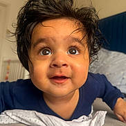 Veer joined the competition — help win amazing prizes! baby, child, curly_hair, wide_eyes, indoor, bedroom, blanket, blue_clothing, expression, face, infant, young_child, soft_light, closeup, portrait, cute, smiling, person, skin, toddler