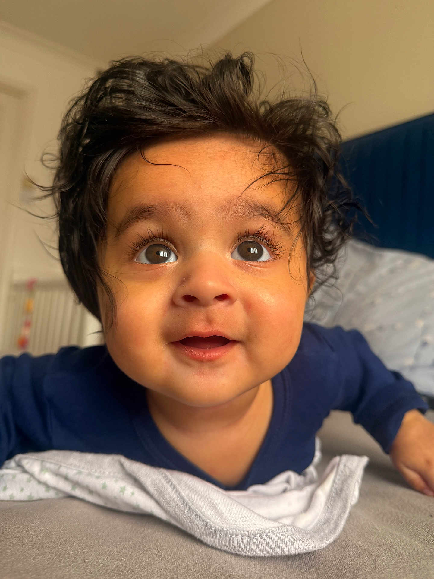 Veer joined the competition — help win amazing prizes! baby, child, curly_hair, wide_eyes, indoor, bedroom, blanket, blue_clothing, expression, face, infant, young_child, soft_light, closeup, portrait, cute, smiling, person, skin, toddler