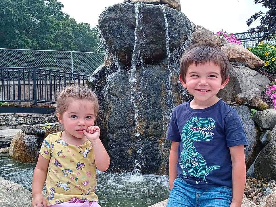Kaylene is registered to the contest to win money with this photo: body_of_water, botany, fountain, fun, grass, green, happy, joy, leisure, nature, people, person, photograph, public_space, recreation, shorts, sky, smile, social_group, toddler