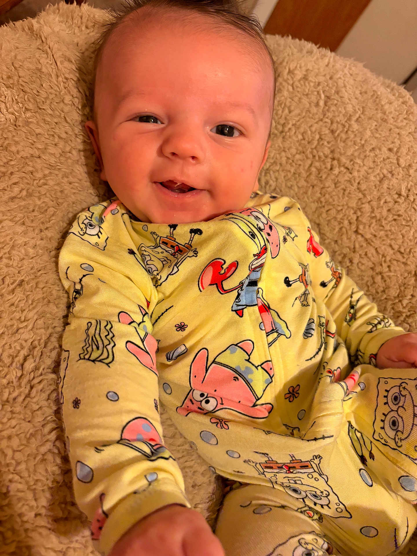 Devon Jr is registered to the contest to win money with this photo: baby, infant, smiling, yellow_clothing, onesie, spongebob, blanket, soft_texture, happy, cute, face, portrait, child, indoor, cozy, hand, young_child, playful, comfort, casual