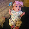 baby, child, infant, portrait, face, eyes, pink_bow, headband, floral_clothing, onesie, pants, bare_feet, fists, sitting, couch, wooden_floor, toy, indoor, living_room, serious_expression