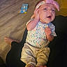 baby, infant, child, smiling, happy, portrait, headband, bow, floral_clothing, onesie, pants, bare_feet, sitting, lap, indoor, wooden_floor, couch, toy, family, close_up