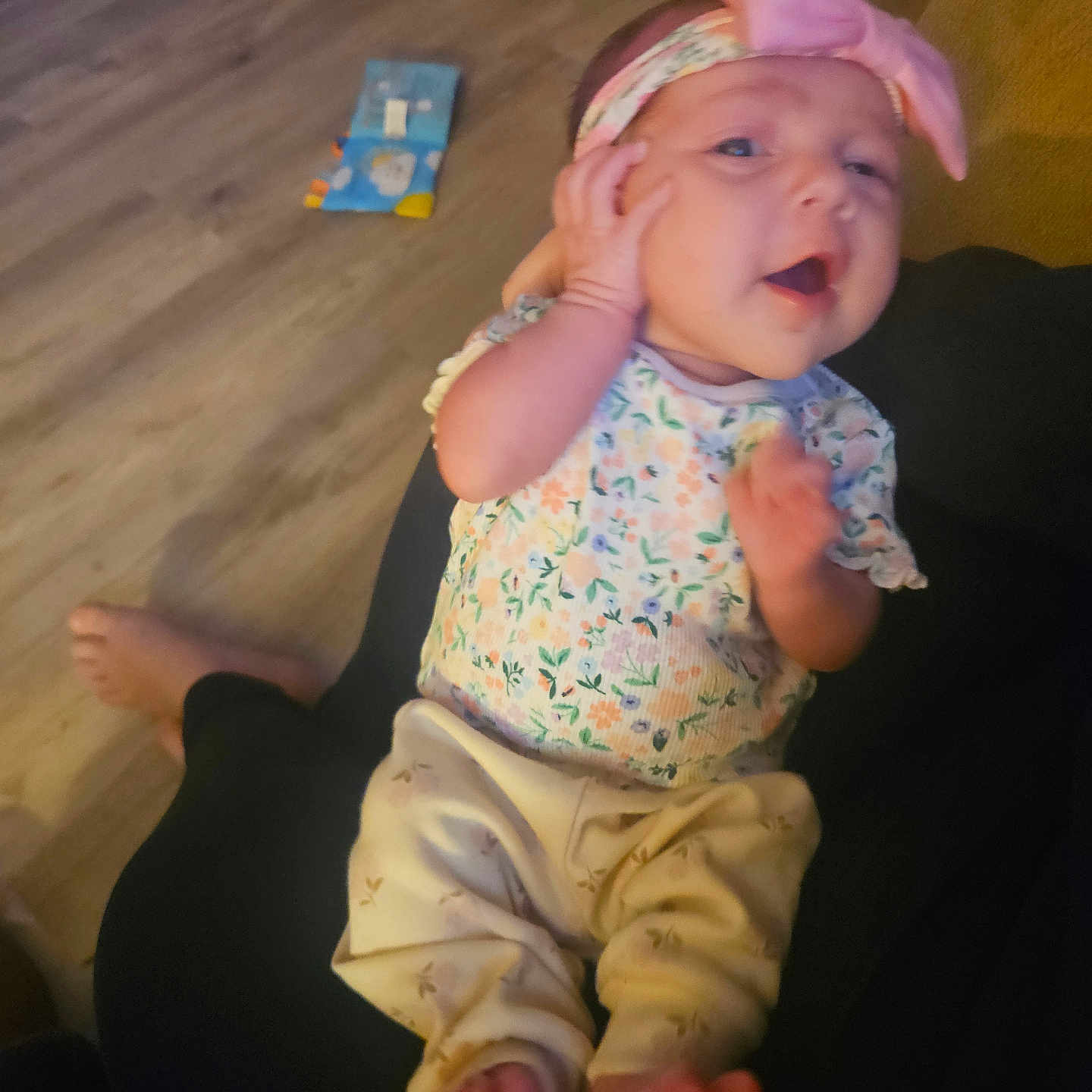 Makayla joined the competition — help win amazing prizes! baby, infant, child, smiling, happy, portrait, headband, bow, floral_clothing, onesie, pants, bare_feet, sitting, lap, indoor, wooden_floor, couch, toy, family, close_up