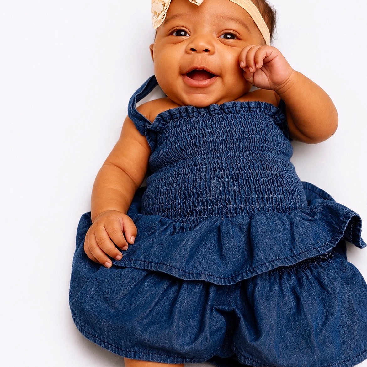 Merci is registered to the contest to win money with this photo: baby, child, smiling, blue_dress, headband, bow, infant, cute, happy, lying_down, white_background, skin, face, hand, footwear, portrait, adorable, young, person, clothing