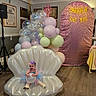 toddler, child, balloon, inflatable, clam_shell, party, birthday, tutu, headband, floor, indoor, decoration, balloon_arrangement, pink, purple, green, celebration, smiling, festive, wood_floor