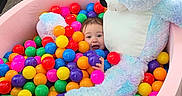Isabella joined the competition — help win amazing prizes! child, ball_pit, teddy_bear, colorful_balls, indoor, carpet, pink_container, toy, play, happy, face, furniture, wooden_cabinet, pastel_colors, soft_toy, baby, smiling, cute, kid, living_room