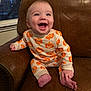 baby, child, pajamas, pumpkin_pattern, smiling, happy, indoor, leather_chair, sitting, cute, infant, portrait, cozy, foot, hand, expression, clothing, face, young_child, home