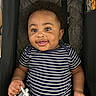 baby, child, smiling, curly_hair, striped_clothing, onesie, pacifier, stroller, cushion, infant, happy, person, indoor, cute, portrait, young, hand, face, playful, comfort