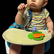 Evren is registered to the contest to win money with this photo: baby, child, high_chair, teether, carrot_toy, striped_shirt, blue_eyes, bare_feet, infant, cute, portrait, expression, sitting, hand, fingers, skin, face, indoor, isolated, background