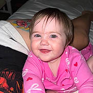 Lorelai is registered to the contest to win money with this photo: baby, child, smiling, pink_clothing, heart_pattern, face, portrait, happy, person, tattoo, bed, indoor, skin, hair, eyes, long_sleeve, infant, cute, reaching, closeup