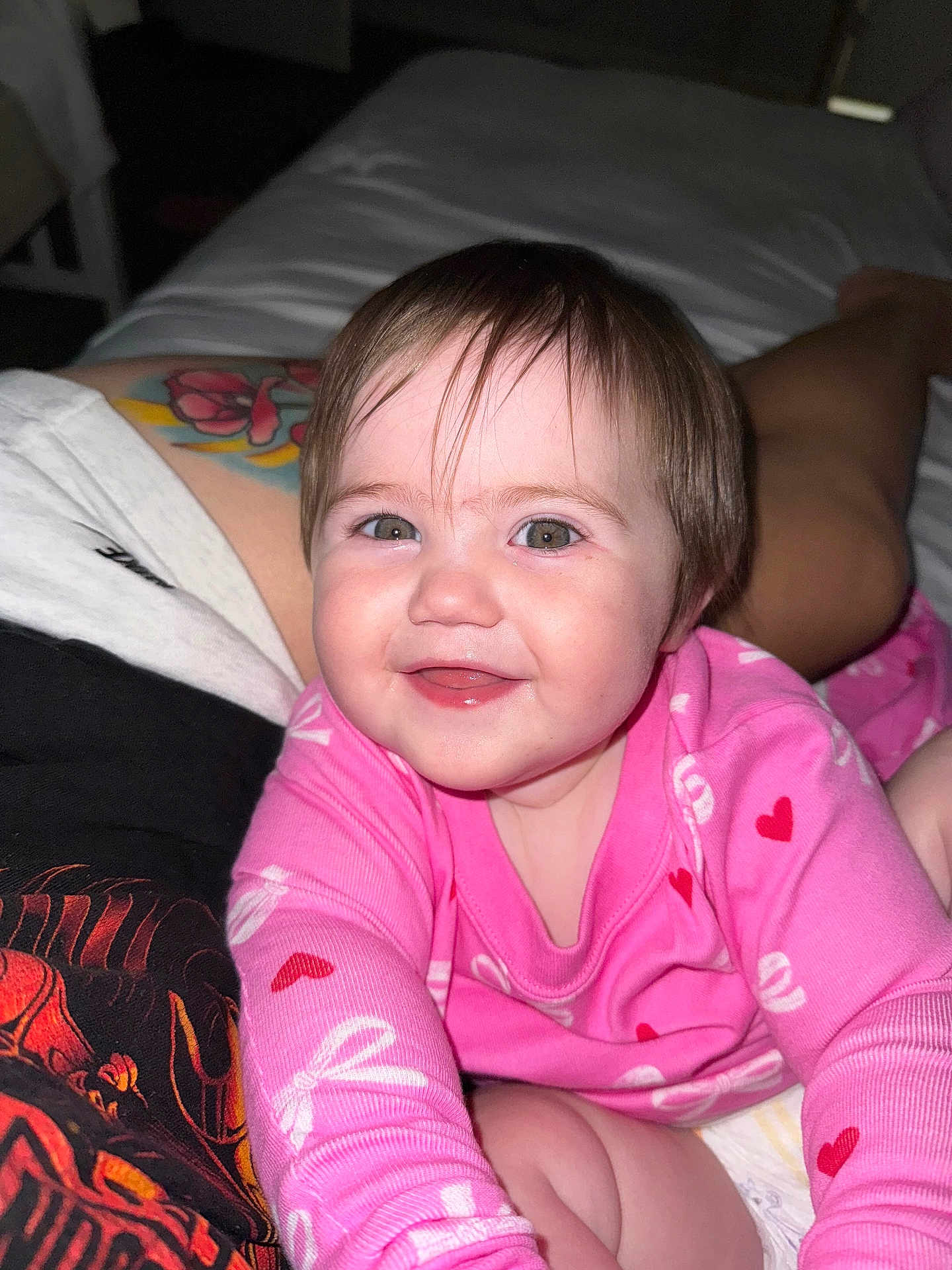 Lorelai is registered to the contest to win money with this photo: baby, child, smiling, pink_clothing, heart_pattern, face, portrait, happy, person, tattoo, bed, indoor, skin, hair, eyes, long_sleeve, infant, cute, reaching, closeup