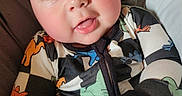 Wylde joined the competition — help win amazing prizes! baby, blue_eyes, child, clasped_hands, close_up, clothing, curious, cute, dinosaur_pattern, hands, indoor, infant, onesie, person, portrait, rosy_cheeks, skin, smiling, soft_bedding, young
