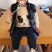Emmanuel a rejoint le concours — aidez-le/la à gagner de superbes lots ! toddler, child, pacifier, sweater, dog_design, vest, sneakers, table, wooden_table, indoor, flooring, chair, wicker_chair, person, cute, smiling, clothing, home, casual, portrait