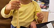 Emmanuel participe au concours pour gagner de l'argent avec cette photo : child, toddler, yellow_shirt, chopsticks, sushi, food, box, table, kitchen, indoor, person, face, brown_hair, expression, hand, seat, curious, eating, casual, home