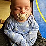 baby, blue_clothing, child, closeup, cozy, cute, door, floral_pattern, hands, holding, indoor, infant, pacifier, person, portrait, relaxed, sleeping, soft_lighting, window, yellow_stripe