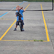 Thomas joined the competition — help win amazing prizes! child, bike, outdoor, concrete, tennis_net, grass, court, smiling, blue_shirt, shorts, sneakers, playful, fence, daylight, young, person, recreation, sport, standing, fun