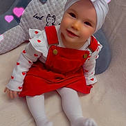 Lucie a rejoint le concours — aidez-le/la à gagner de superbes lots ! baby, child, red_dress, white_turban, flower_headwear, heart_effects, smiling, sitting, blanket, soft_fabric, indoors, cute, portrait, infant, white_tights, happy, cozy, baby_clothes, playful, couch