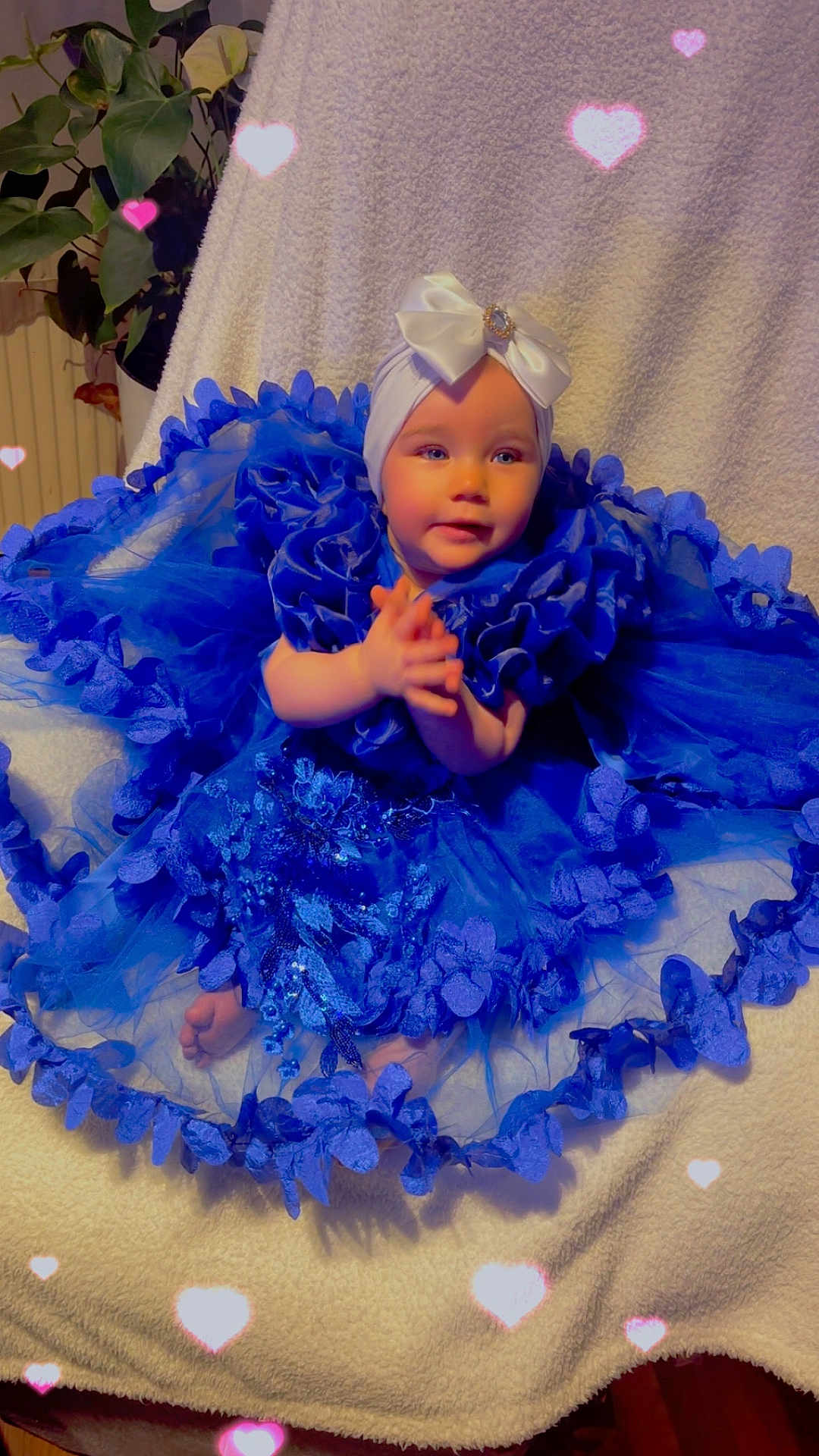 Lucie a rejoint le concours — aidez-le/la à gagner de superbes lots ! baby, blue_dress, headwrap, bow, frills, sitting, blanket, hearts, cute, indoors, plant, decor, portrait, child, smiling, soft_lighting, fabric, tulle, adorable, happy