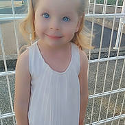 Lucie participe au concours pour gagner de l'argent avec cette photo : child, girl, smiling, white_top, skirt, pink_hair_ties, fence, outdoor, daylight, concrete, playground, blue_eyes, standing, person, happy, casual_clothing, hair, young, cute, portrait