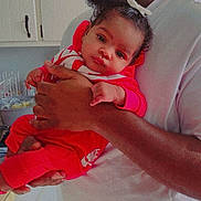 Marjae is registered to the contest to win money with this photo: baby, infant, red_clothing, nike, person, adult_hand, kitchen, cabinet, countertop, dishrack, curly_hair, casual, indoor, portrait, holding, calm, looking_at_camera, white_shirt, skin_tone, close_up