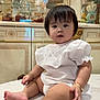 baby, child, infant, white_clothing, bracelet, balloon, princess_balloon, crown_balloon, indoor, marble_surface, decor, glass_cabinet, gold_detail, cute, portrait, sitting, curious, chubby_cheeks, short_hair, festive