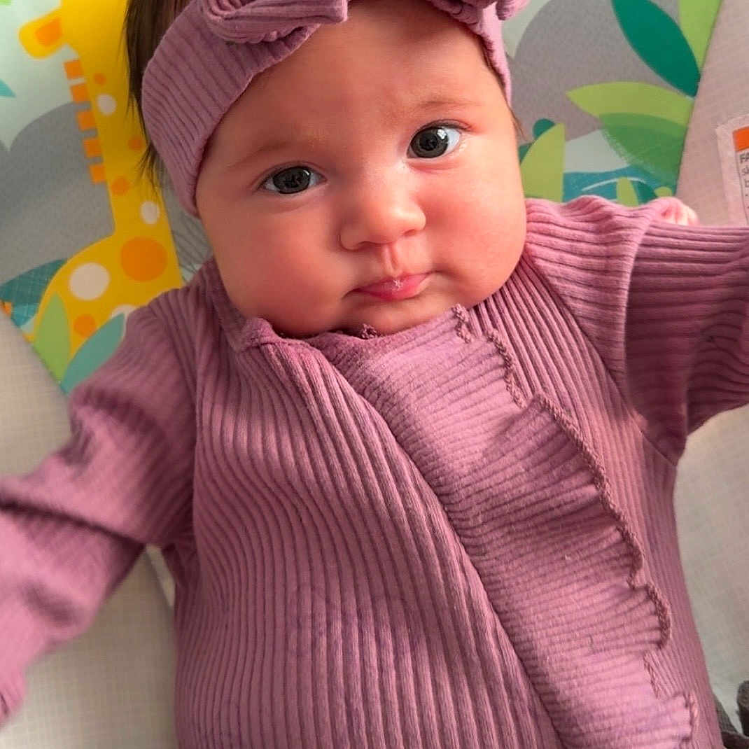 Ramsey is registered to the contest to win money with this photo: baby, infant, child, headband, bow, pink_clothing, ribbed_fabric, giraffe_illustration, baby_seat, face, cheeks, eyes, portrait, cute, indoors, expression, clothing, person, closeup, baby_gear