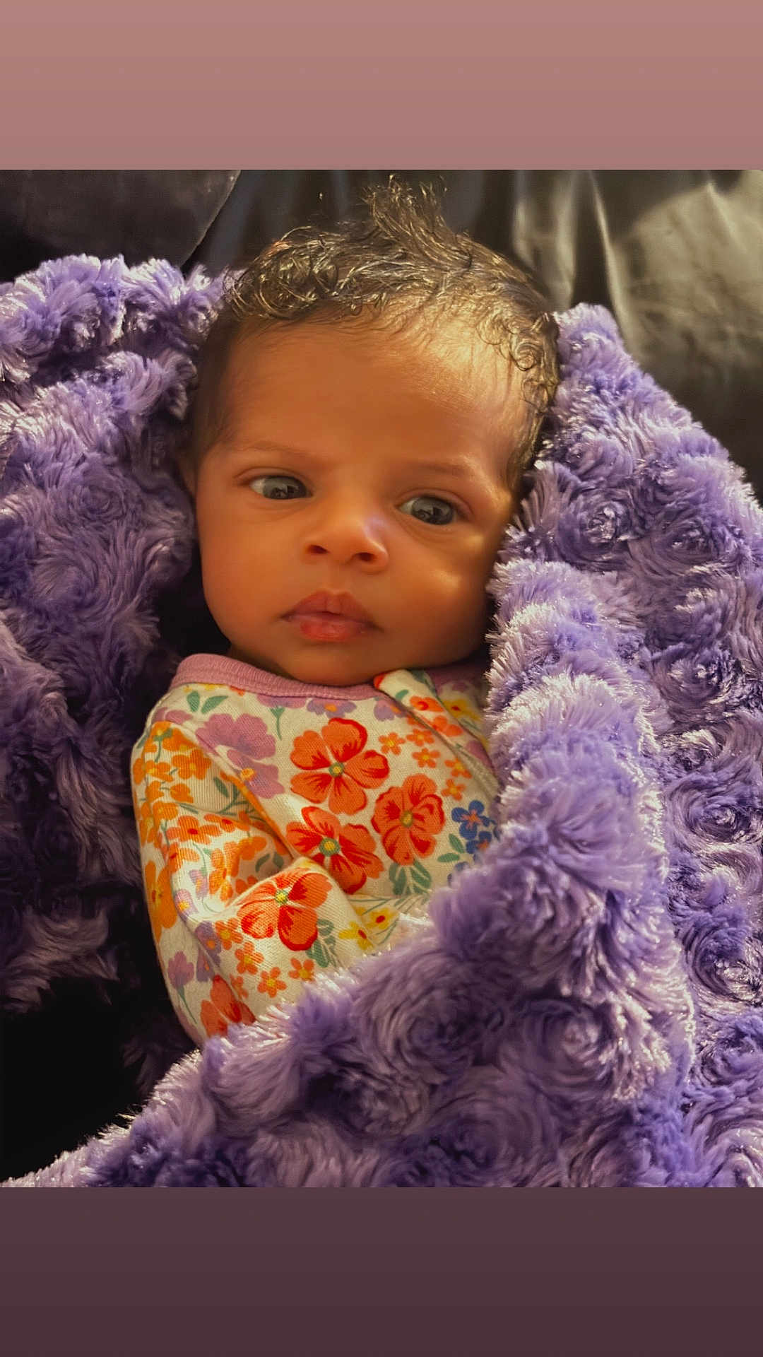 Ocean joined the competition — help win amazing prizes! baby, infant, blanket, purple, floral_onesie, curly_hair, face, cute, wrapped, sleepwear, child, portrait, soft_texture, warm, newborn, expression, cozy, person, indoors, resting