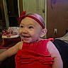 baby, child, smiling, red_dress, headband, indoor, happy, infant, person, cute, playful, furniture, room, baby_walker, toothy_grin, portrait, seated, clothing, face, joyful