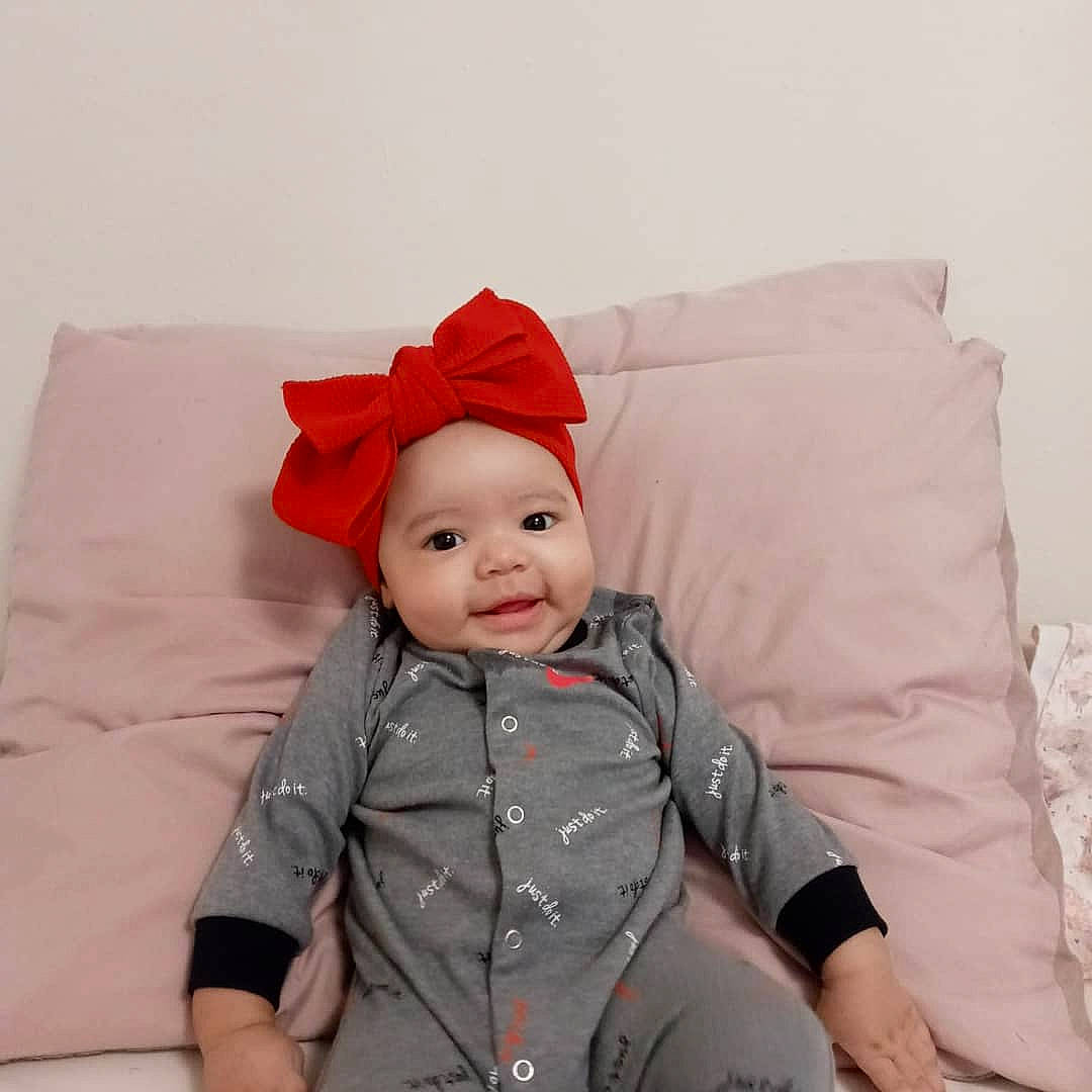 Zendaya is registered to the contest to win money with this photo: baby, baby_toddler_clothing, cap, carmine, child, comfort, costume_hat, face, happy, hat, head, headwear, human_body, linens, person, pillow, sitting, sleeve, smile, t_shirt
