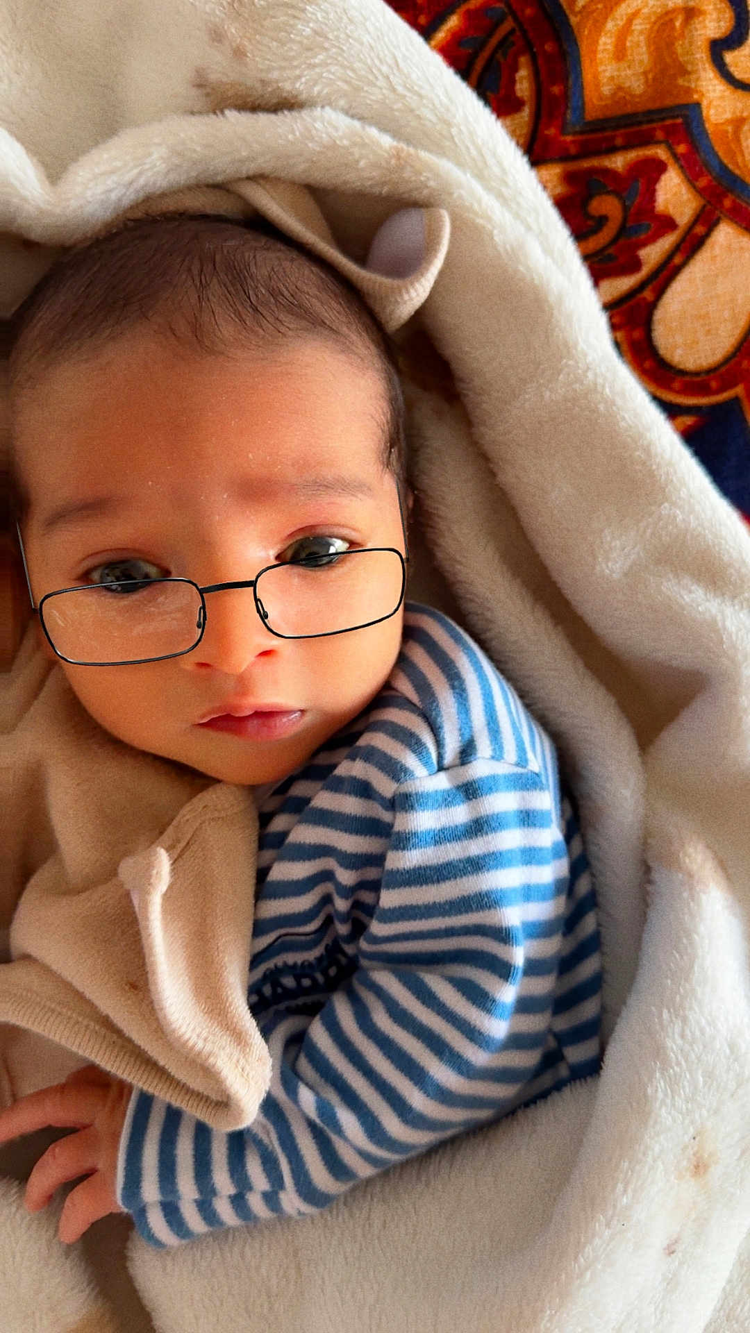 Mhiirr is registered to the contest to win money with this photo: baby, infant, glasses, blanket, striped_clothing, soft_texture, cute, portrait, closeup, sleepy_eyes, cozy, hand, face, newborn, indoors, warm, child, young, resting, wrapped